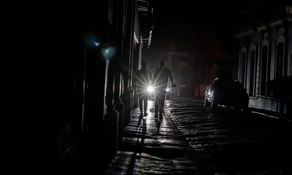 Residents walking a dark street with flashlights during a hurricane power outage